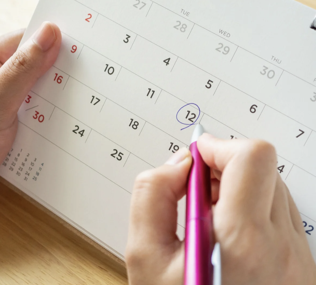 Main dans un calendrier, surlignant une date avec un stylo rose.