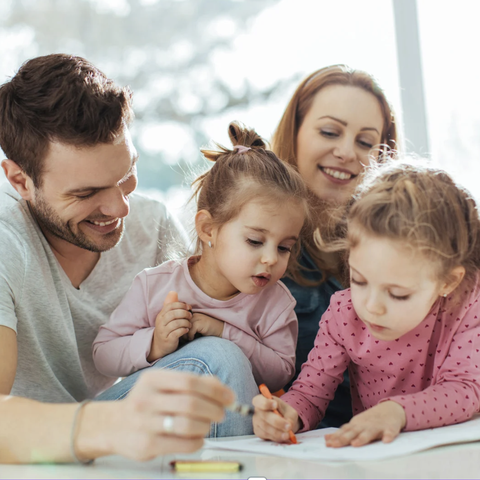 Une famille joyeuse dessine ensemble, deux enfants et leurs parents, dans un environnement lumineux.