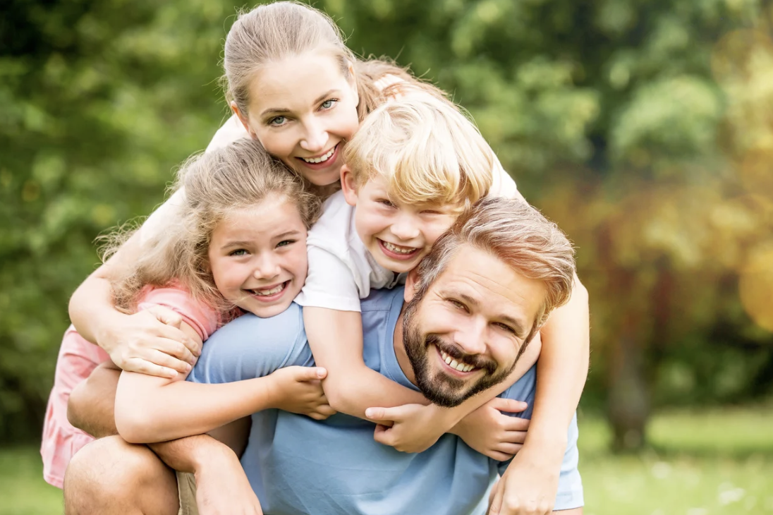 Une famille souriante avec deux enfants, jouant dans un parc verdoyant.