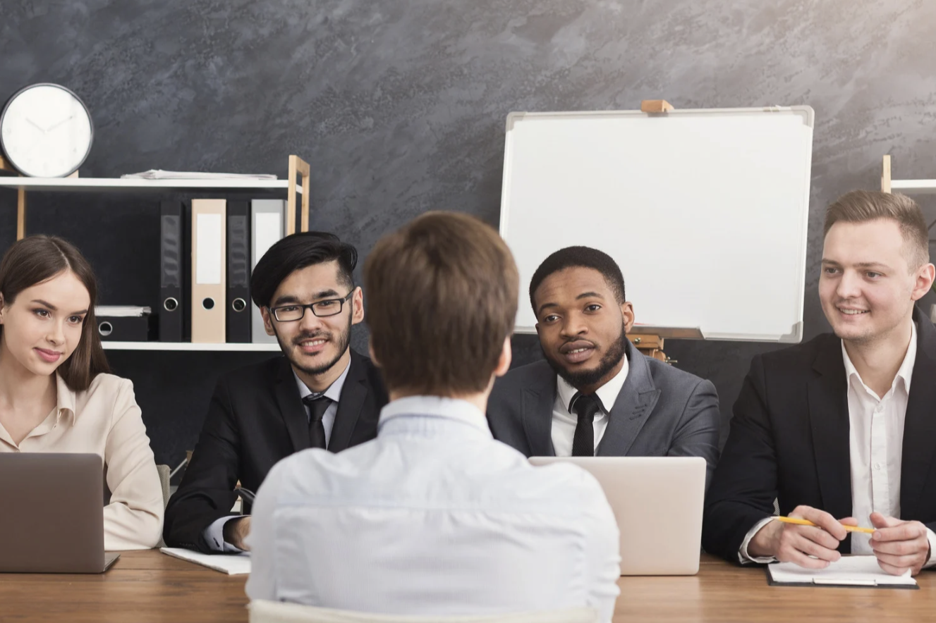Groupe de personnes en réunion, discutant autour d'une table, avec un tableau en arrière-plan.