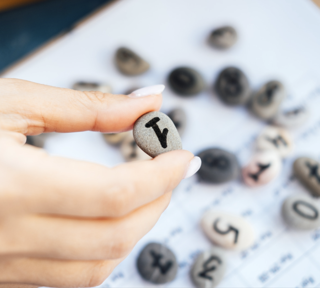 Main tenant une pierre marquée d'un chiffre, entourée de plusieurs autres pierres similaires.