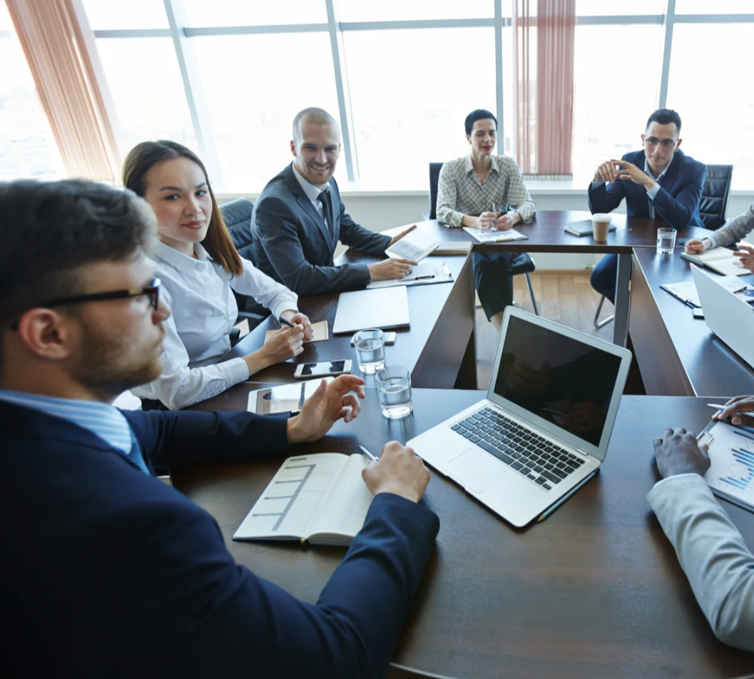 Groupe de professionnels en réunion autour d'une table, avec ordinateurs portables et documents.